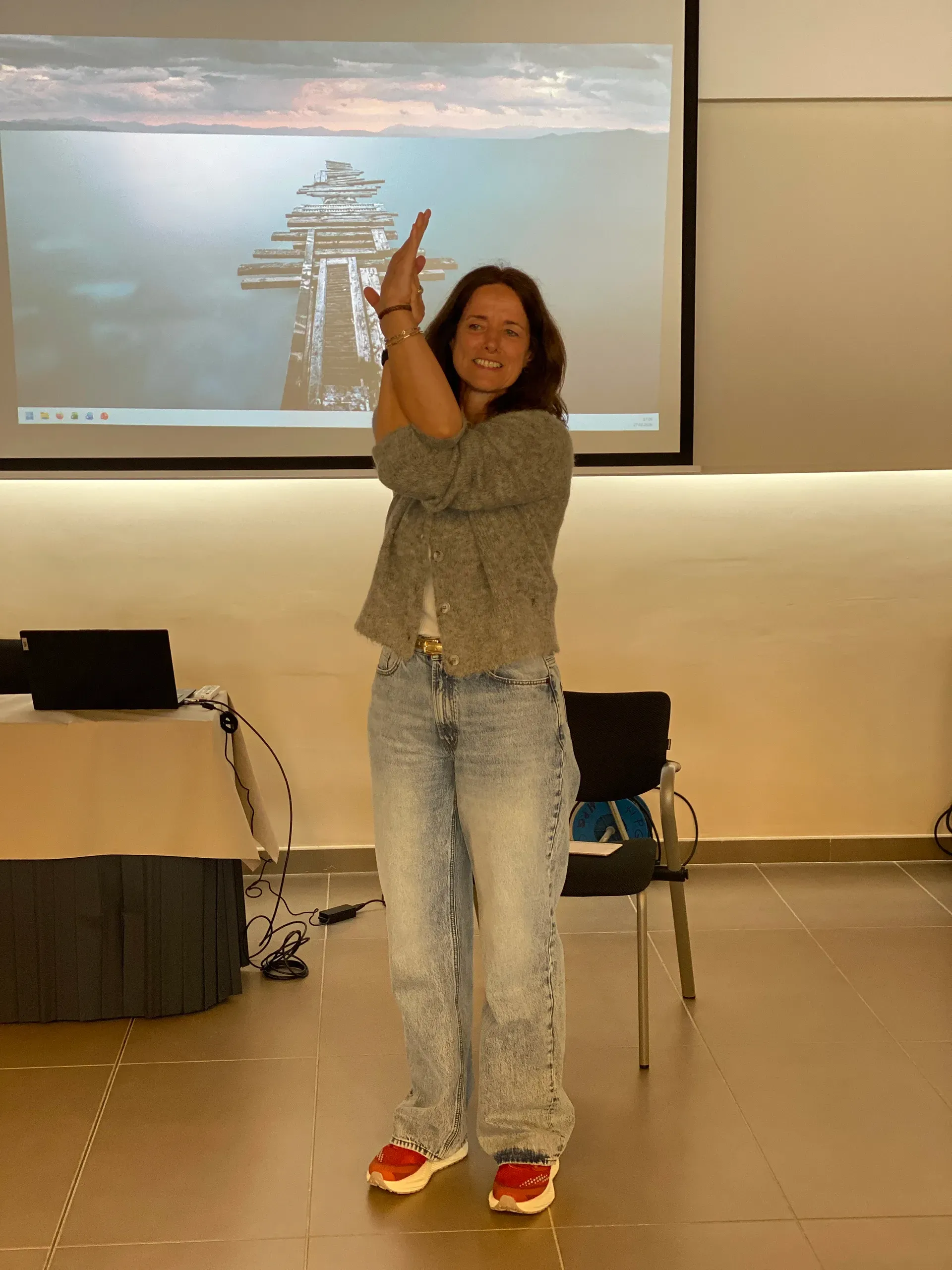 Eine Frau steht vor einer Projektionsfläche und hält die Arme in einer Yoga-Pose vor dem Gesicht verschränkt.