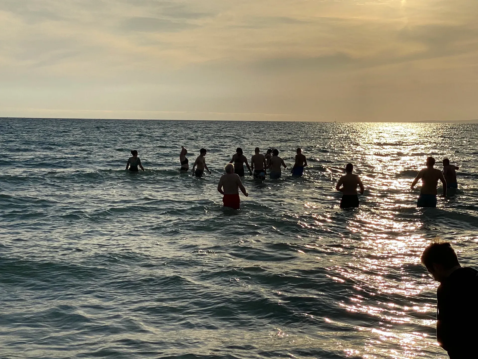 Silhouetten zeichnen sich im hellen Sonnenuntergang ab und waten in die Wellen des Ozeans.