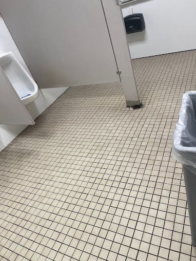 A bathroom with a urinal and a trash can on the floor.