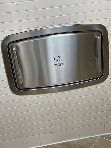 A stainless steel diaper changing station is mounted to a tiled wall.