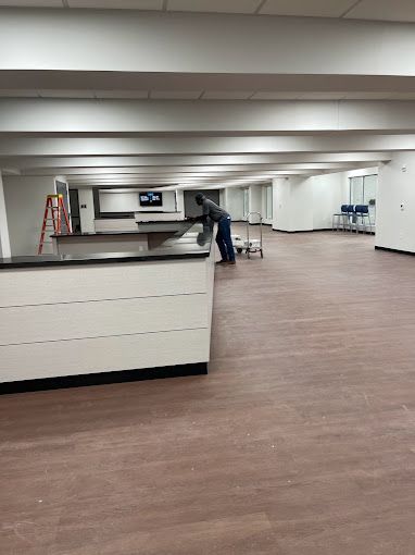 A man is standing in a large empty room with a wooden floor.