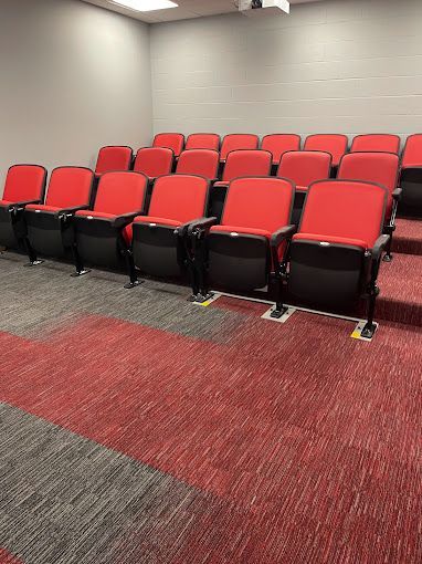 A row of red chairs in an auditorium with a red carpet.