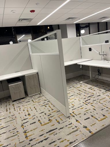 A cubicle with two desks and a rug in an office.