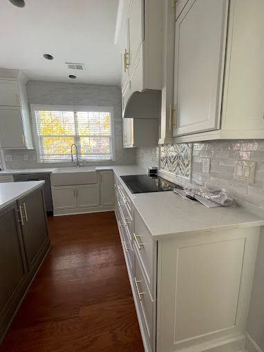 A kitchen with white cabinets , a sink , a stove and a window.
