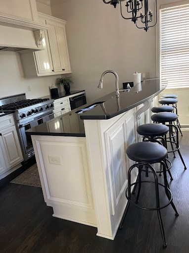 A kitchen with white cabinets and black counter tops and stools.