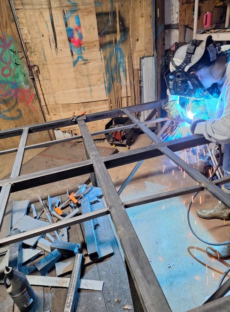 A man is welding a metal frame in a garage.