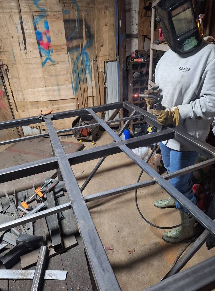 A man wearing a welding mask is working on a piece of metal.