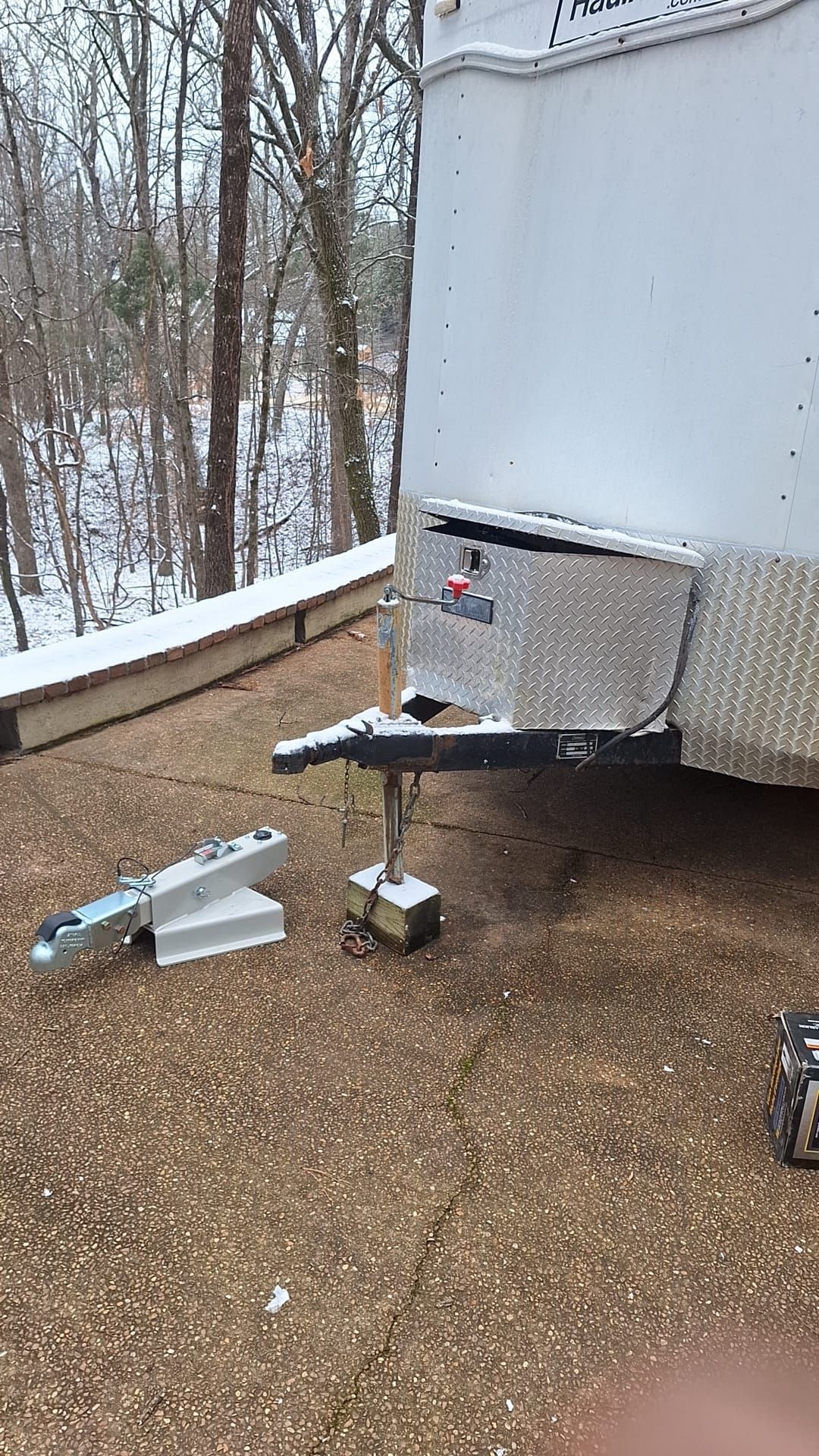 A trailer is parked on a gravel driveway next to a snowy forest.
