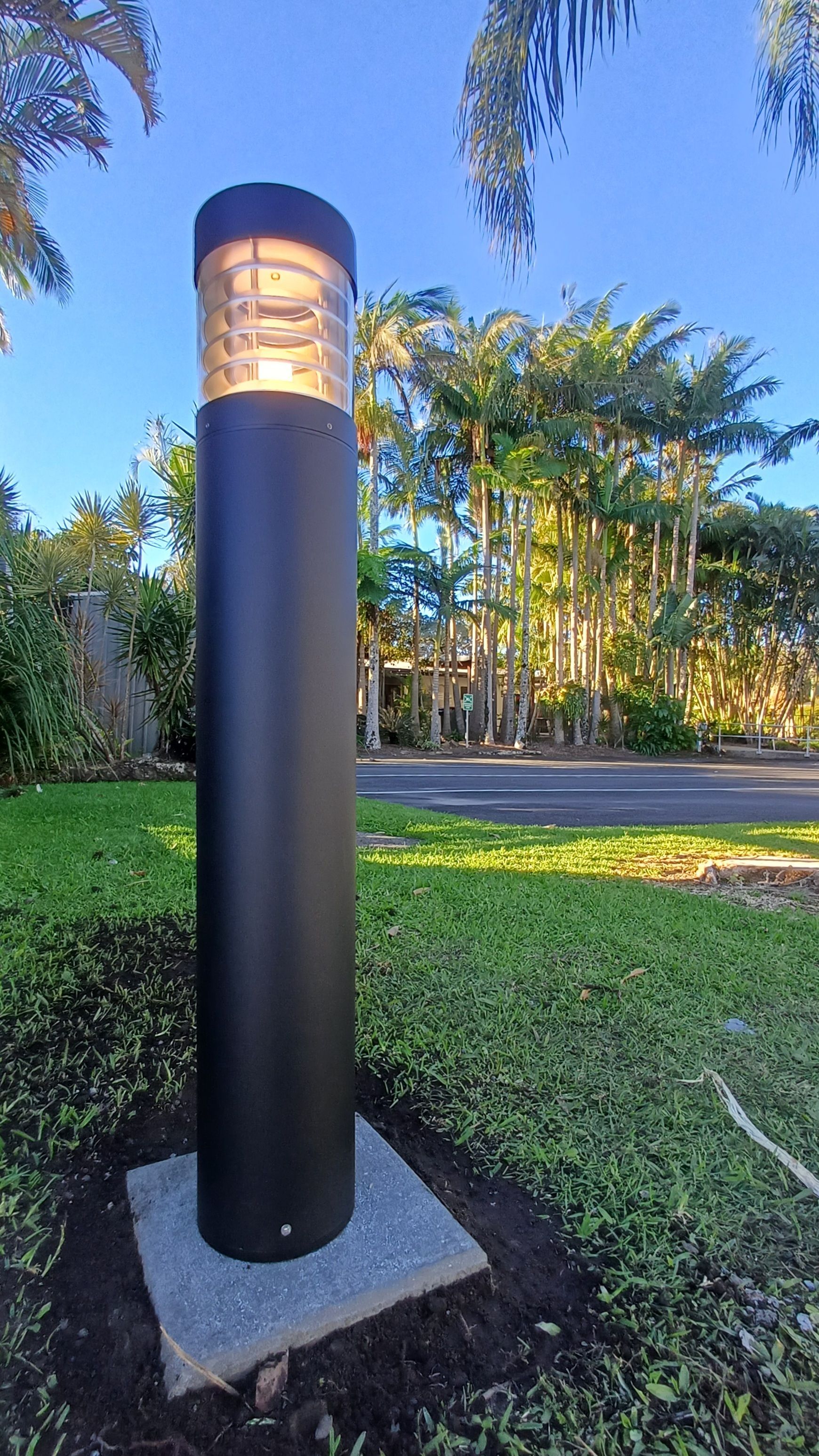 Black walkway lamp on a concrete base beside grass and trees at dusk