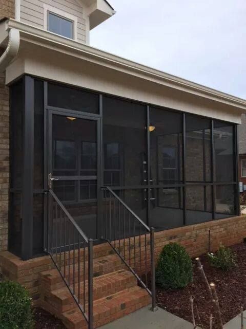 Screened-in porch with brick steps, dark metal railing, and a black-framed screen door and windows.