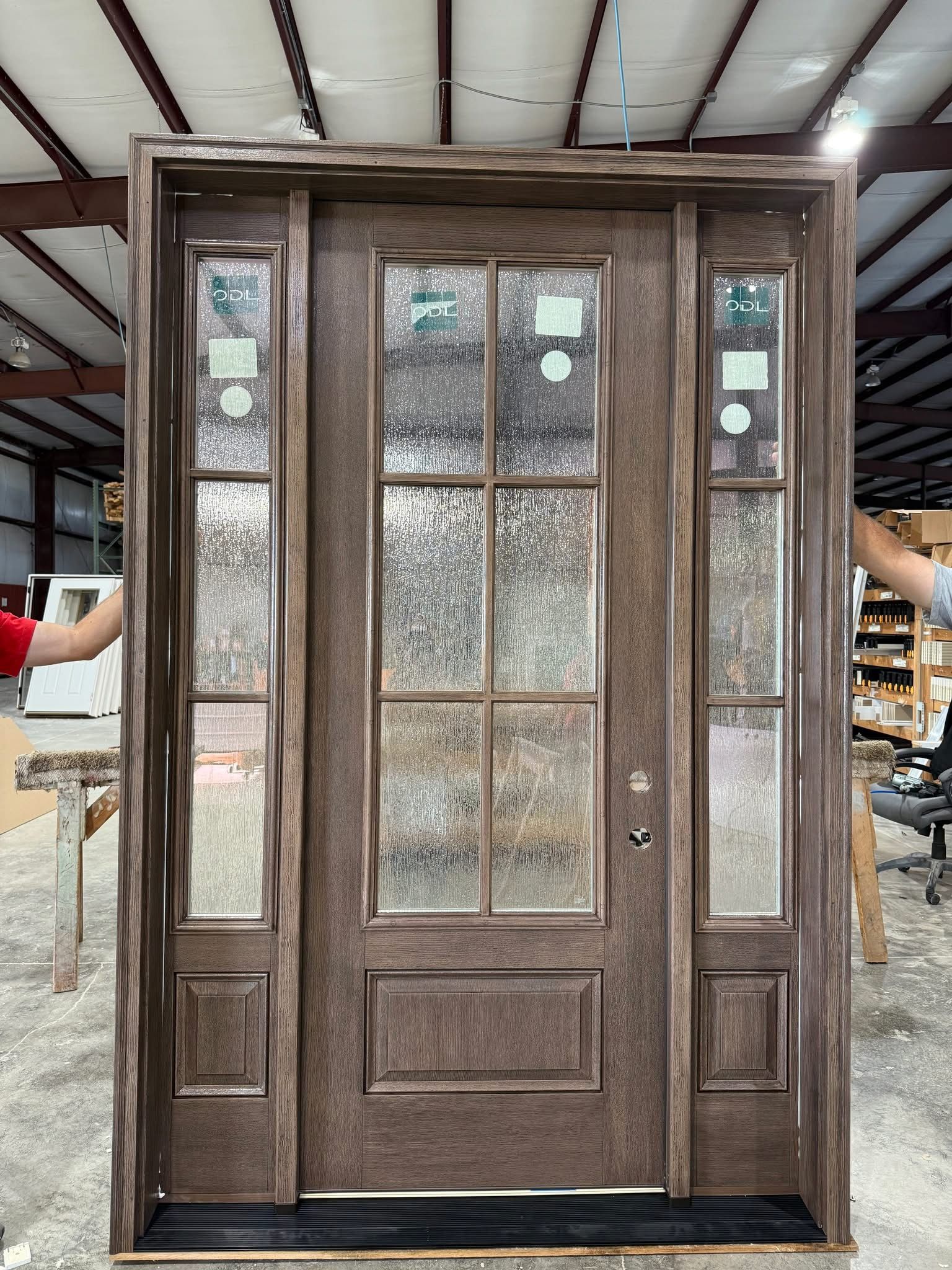 Brown front door with sidelights, featuring textured glass panels. Held vertically by two unseen hands.