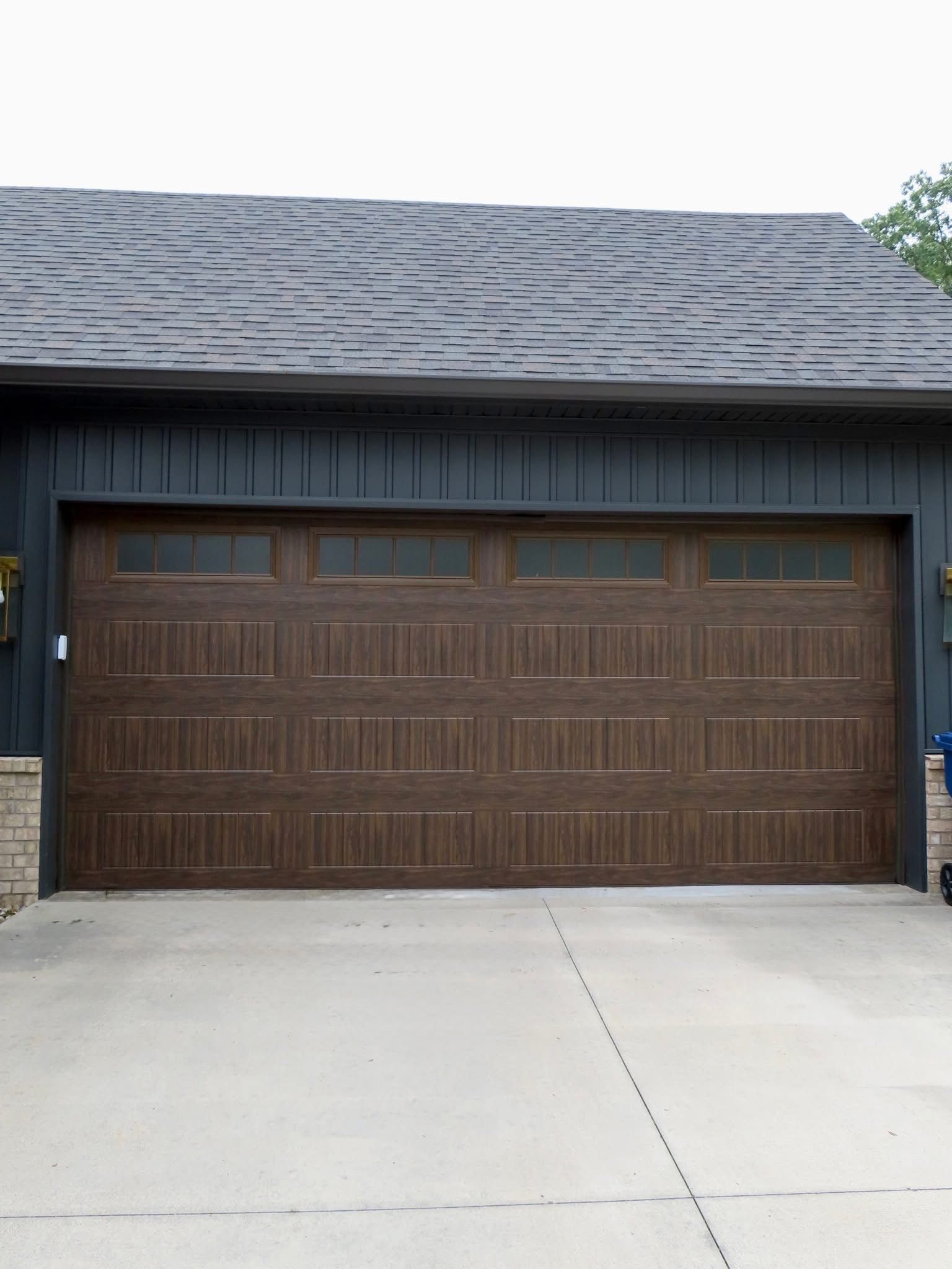 Brown garage door with windows, blue-gray siding, and gray concrete driveway.