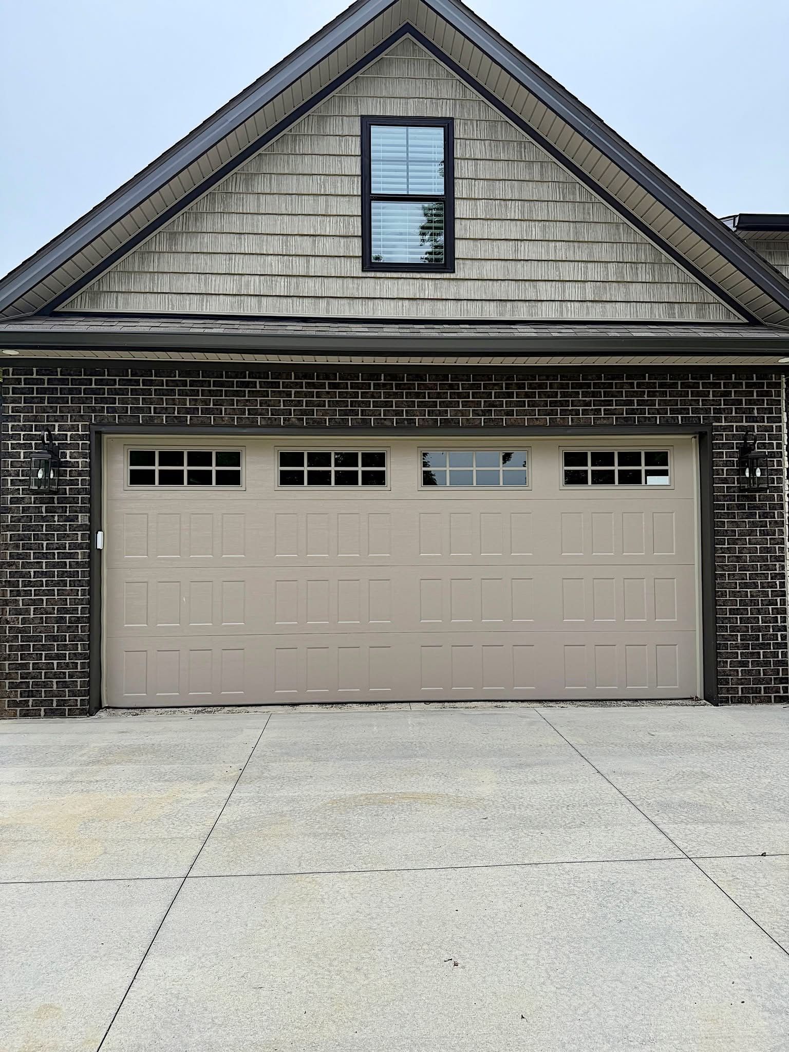 Tan garage door with small windows, beneath a shingled roof and a smaller window.