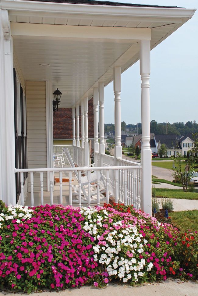 White porch with flowers and rocking chairs, suburban neighborhood in the background.