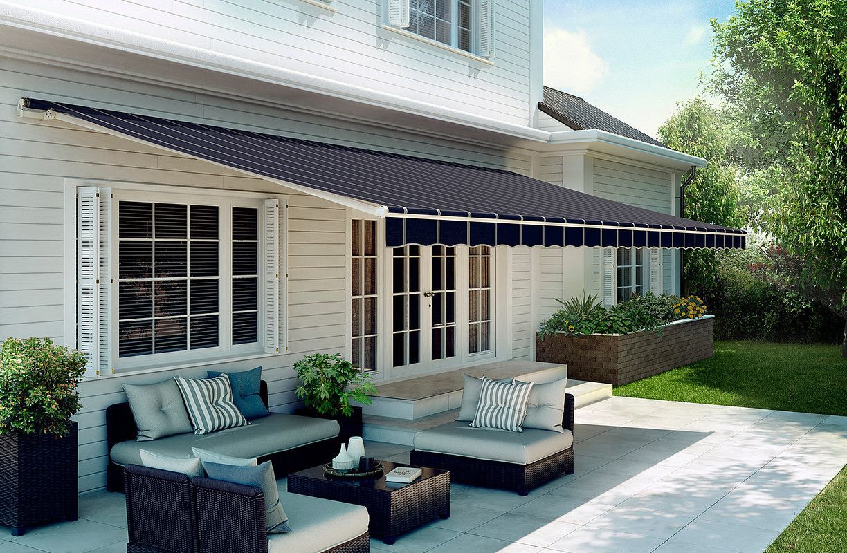 A white house with a patio, featuring outdoor furniture beneath a dark awning.