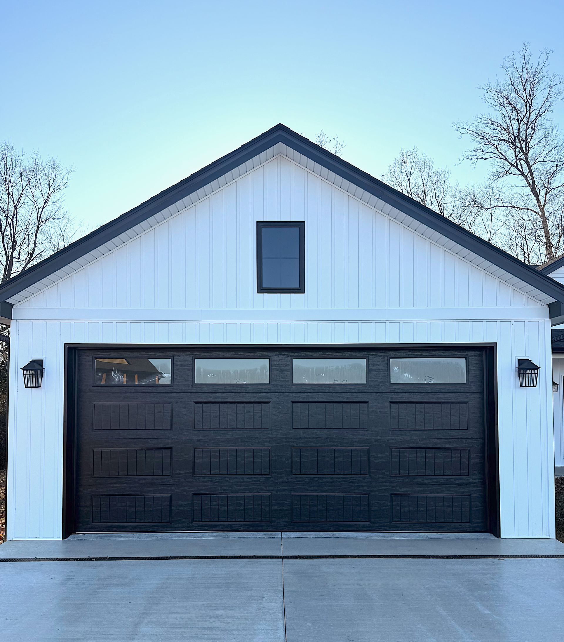 White barn-style garage with a black door and trim, a small window, and two black sconces.
