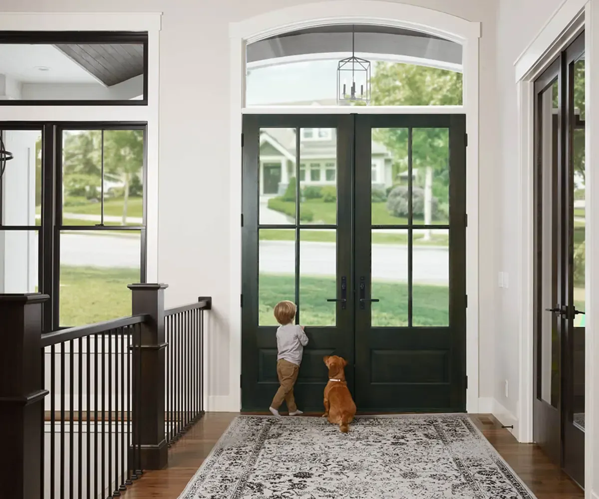 Child and dog looking out a front door with glass panels.