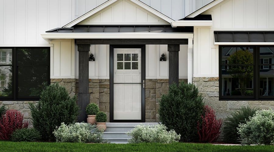 Front door with screen door, flanked by bushes and lamps on a brick facade.