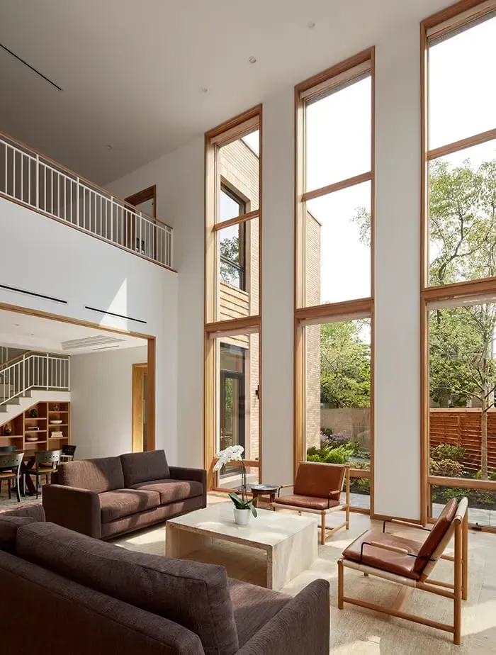 Bright living room with tall windows, two brown sofas, and leather chairs.