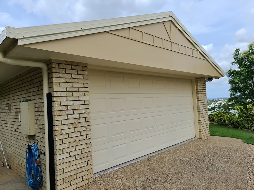 A White Garage Door is on the Side of a Brick Building — BK Painting & Property Maintenance in Gracemere, QLD