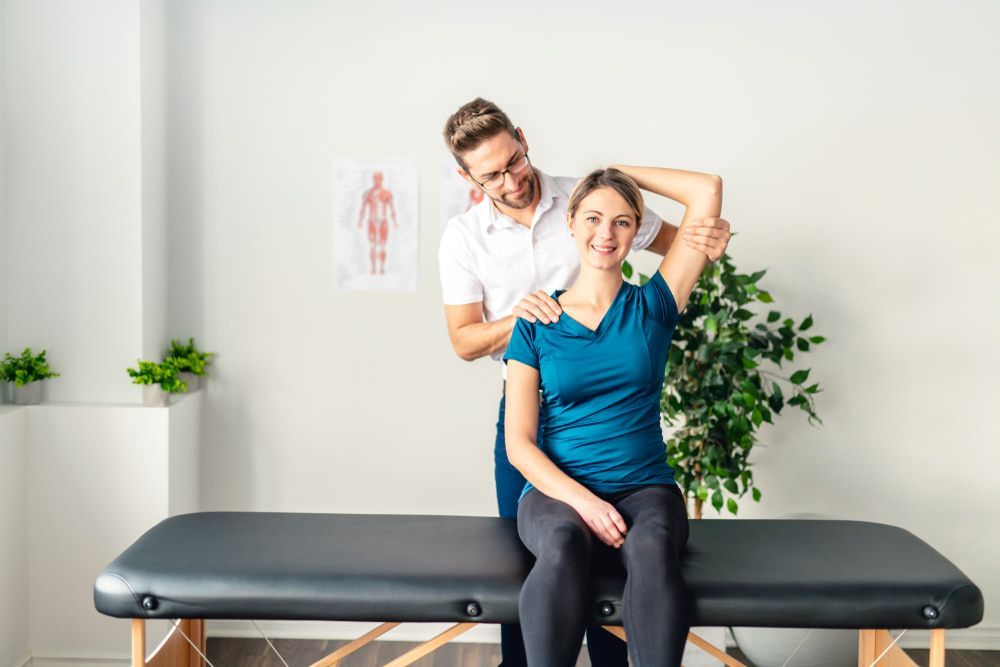 A Man Is Stretching a Woman 's Neck While She Sits on A Table — Illawarra Sports Injury Rehabilitation and Physiotherapy Centre in Bellambi, NSW