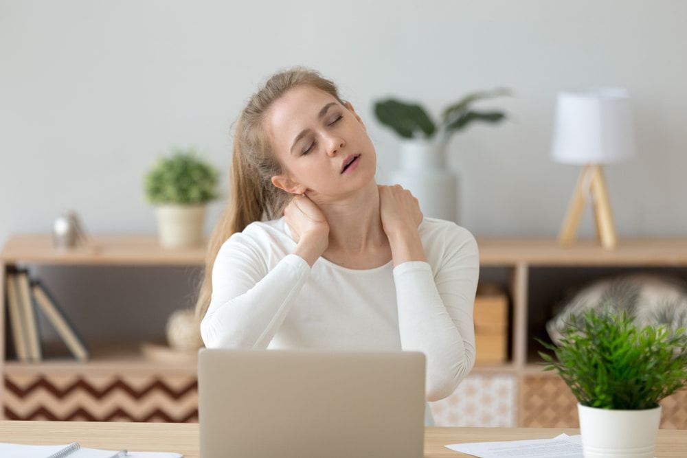 A Woman Is Sitting at A Desk with A Laptop and Holding Her Neck — Illawarra Sports Injury Rehabilitation and Physiotherapy Centre in Bellambi, NSW