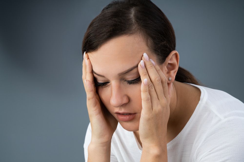 A Woman Is Holding Her Head in Her Hands — Illawarra Sports Injury Rehabilitation and Physiotherapy Centre in Bellambi, NSW