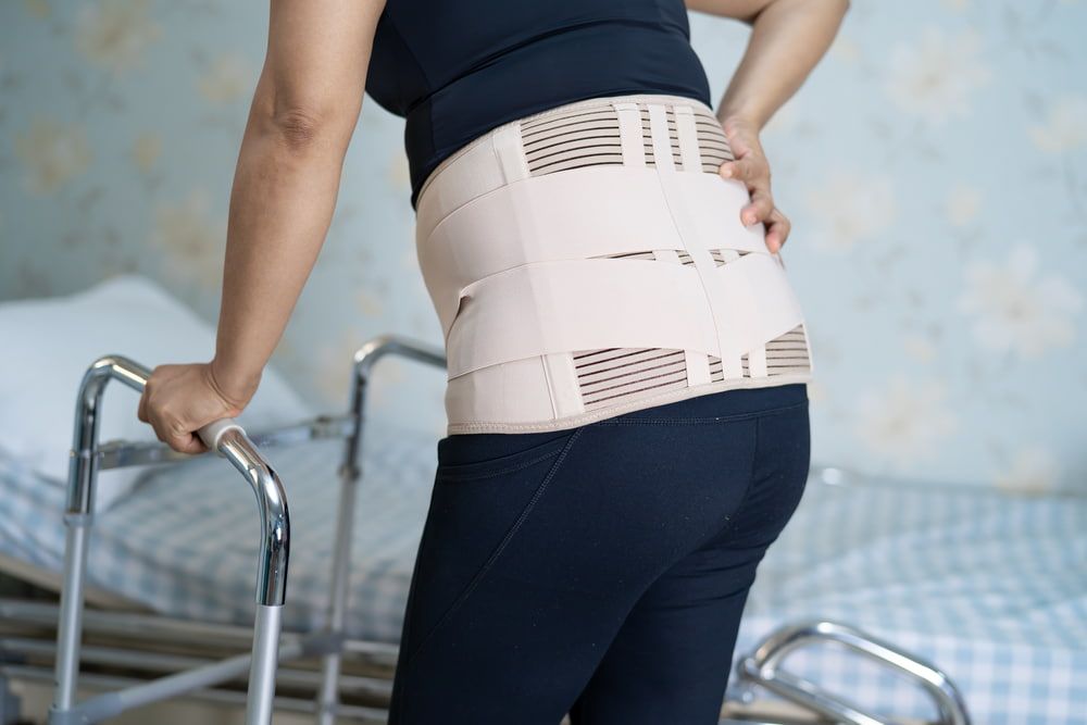 A Woman Wearing a Lumbar Support Belt Is Standing Next to A Walker — Illawarra Sports Injury Rehabilitation and Physiotherapy Centre in Bellambi, NSW