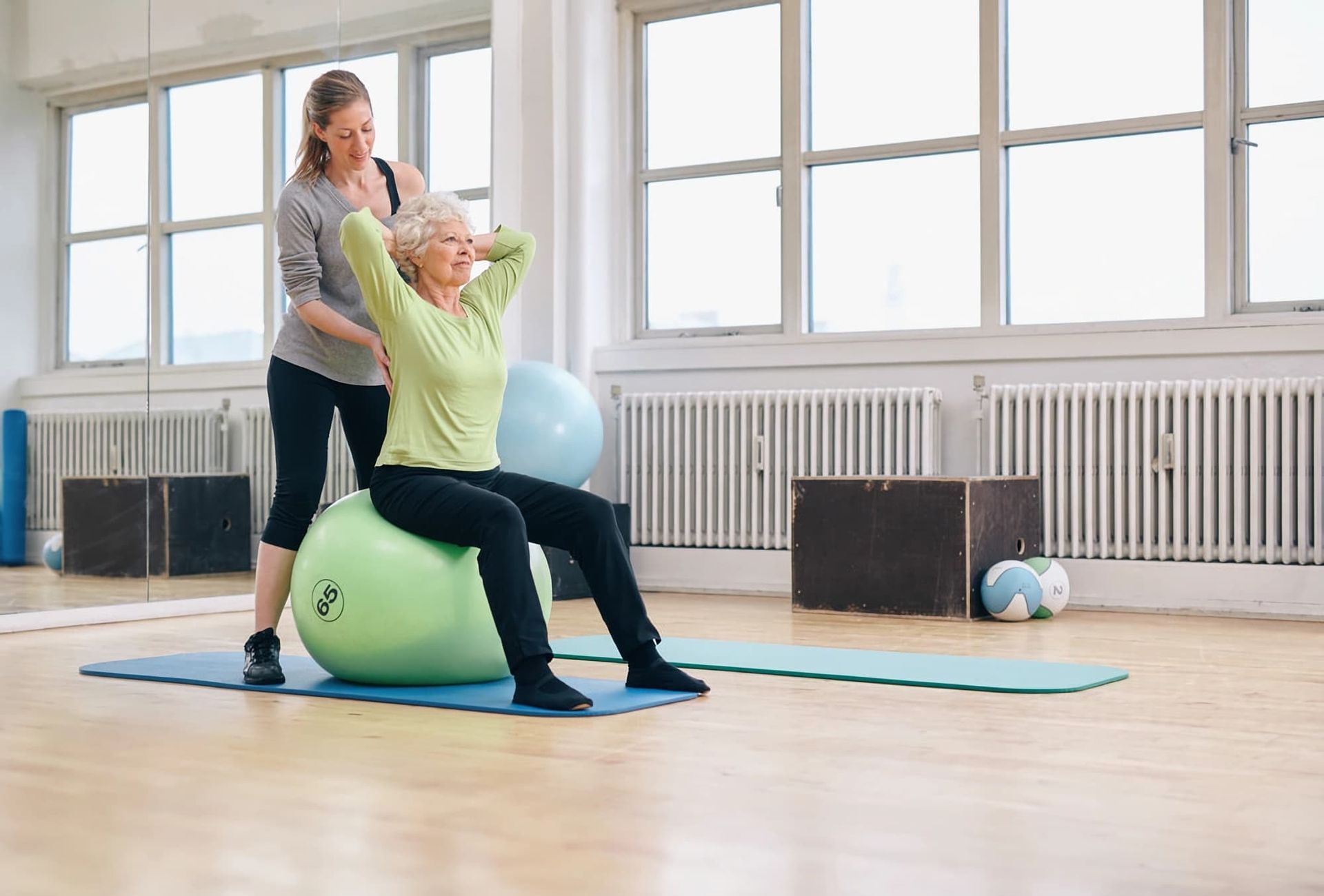 A Woman Is Helping an Older Woman Do Exercises on A Pilates Ball — Illawarra Sports Injury Rehabilitation and Physiotherapy Centre in Bellambi, NSW