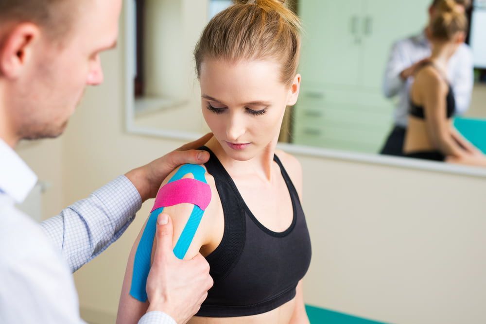 A Man Is Putting Kinesio Tape on A Woman 's Shoulder — Illawarra Sports Injury Rehabilitation and Physiotherapy Centre in Bellambi, NSW