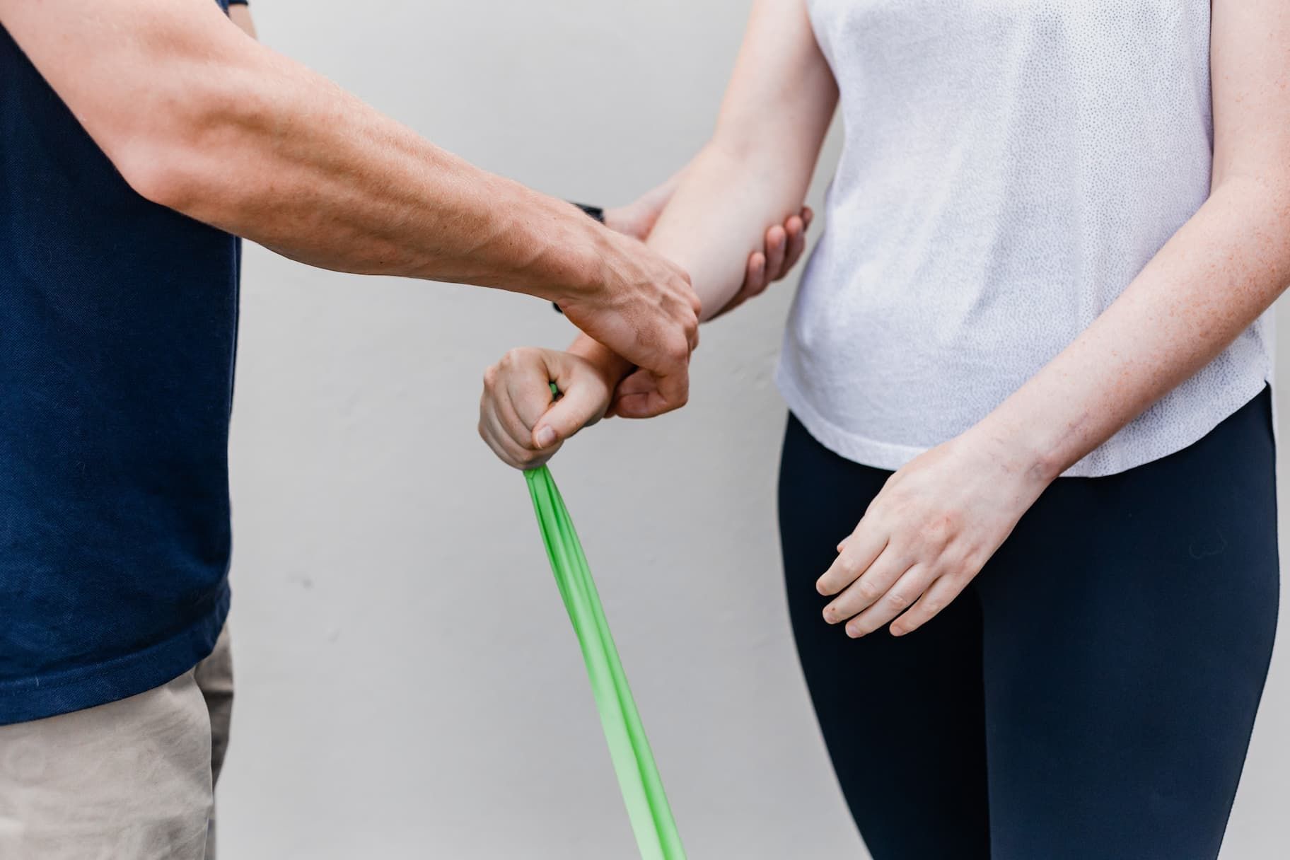 A Man Is Helping a Woman Stretch Her Arm with A Green Resistance Band — Illawarra Sports Injury Rehabilitation and Physiotherapy Centre in Bellambi, NSW