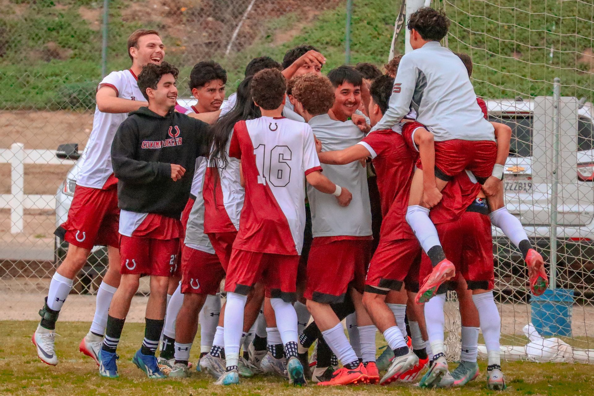 Soccer players in red and white celebrate a goal together on the field.