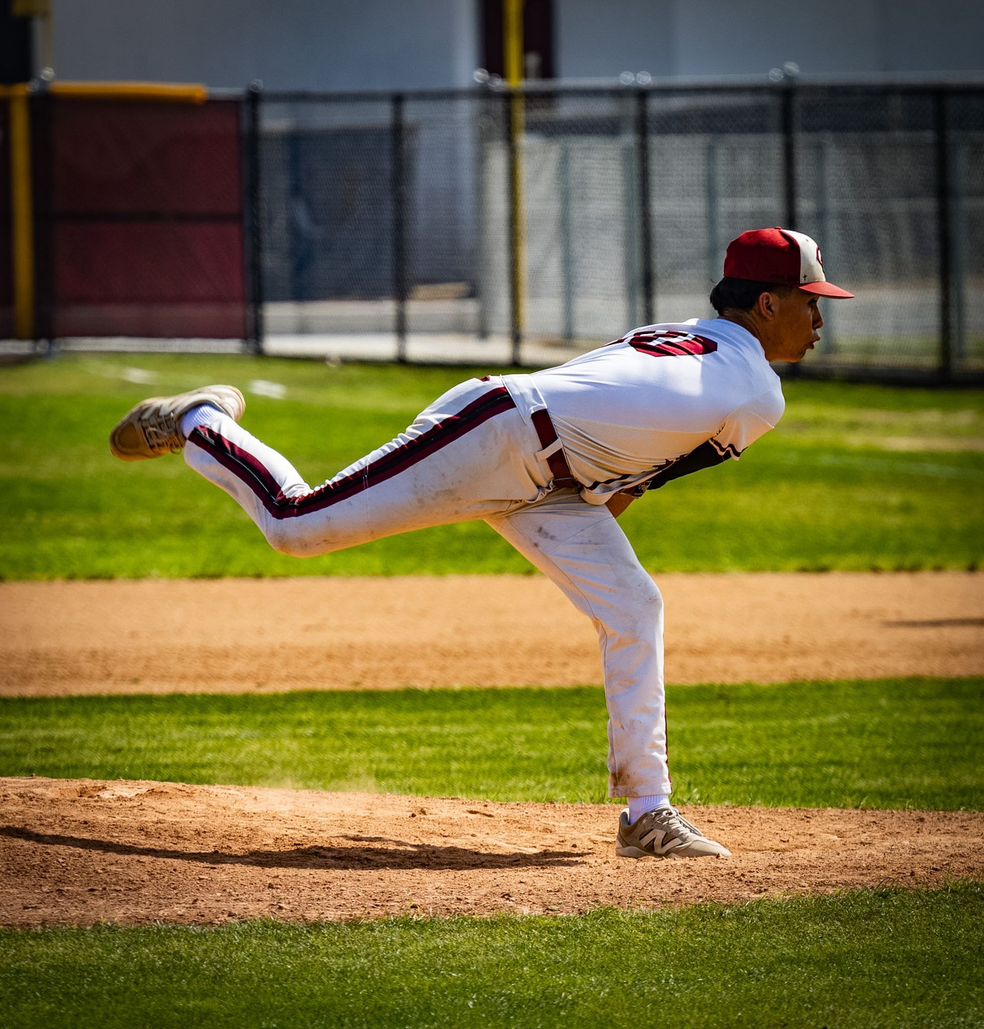 Baseball pitcher in white and red uniform mid-throw on the mound during a game.