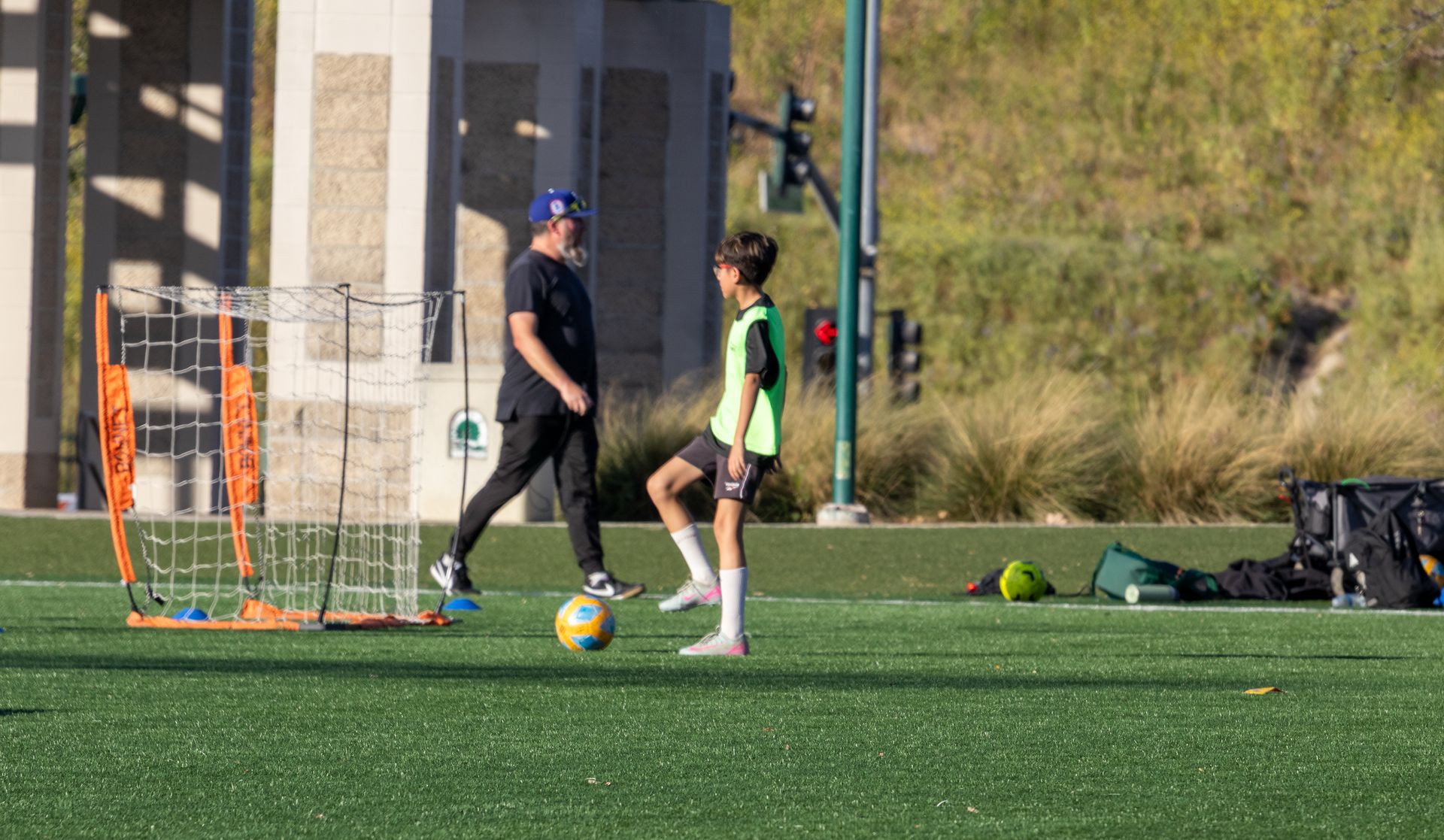 Two athletes on a soccer field passing a ball near the goal at practice