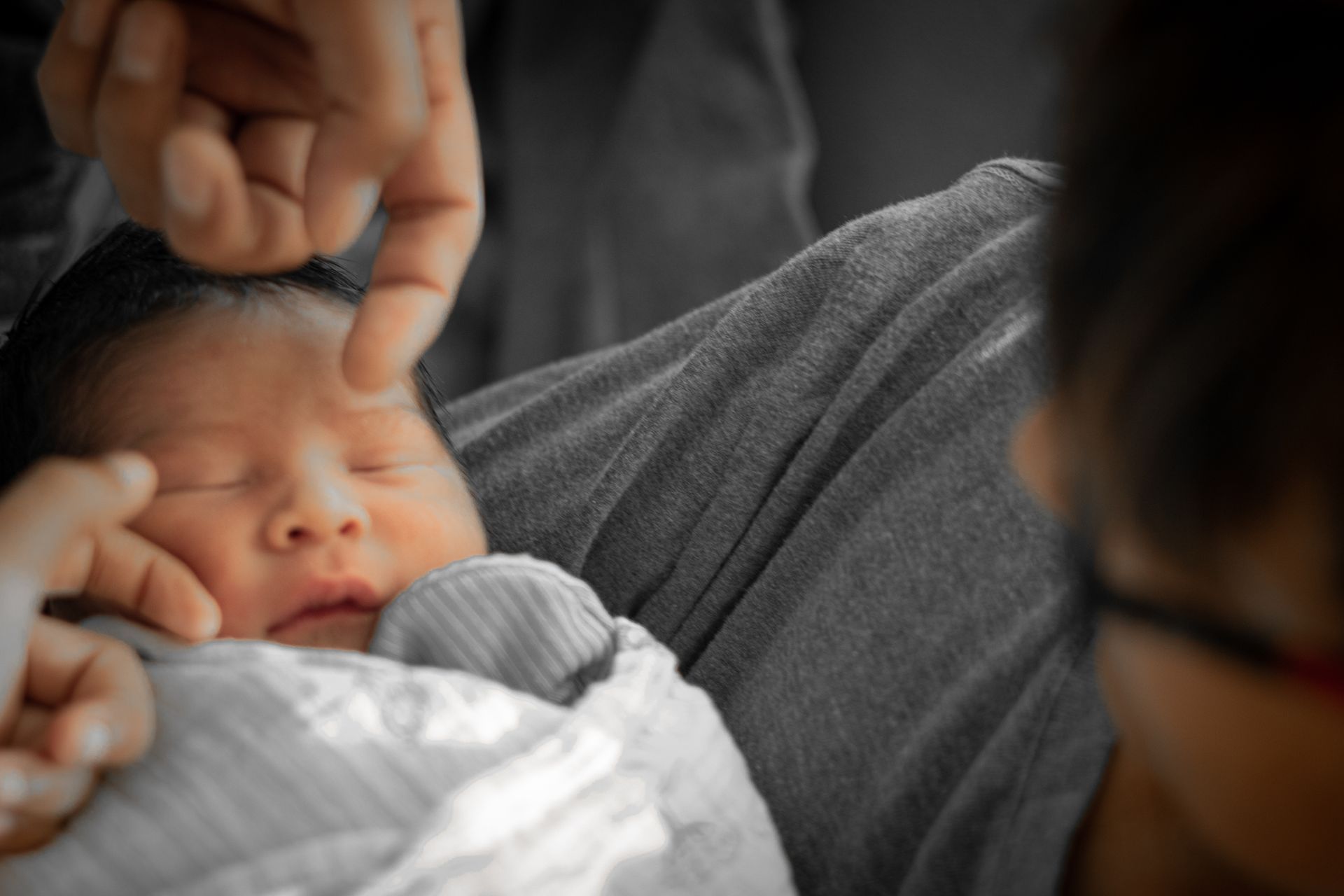 Adult gently touching a sleeping baby wrapped in a gray blanket