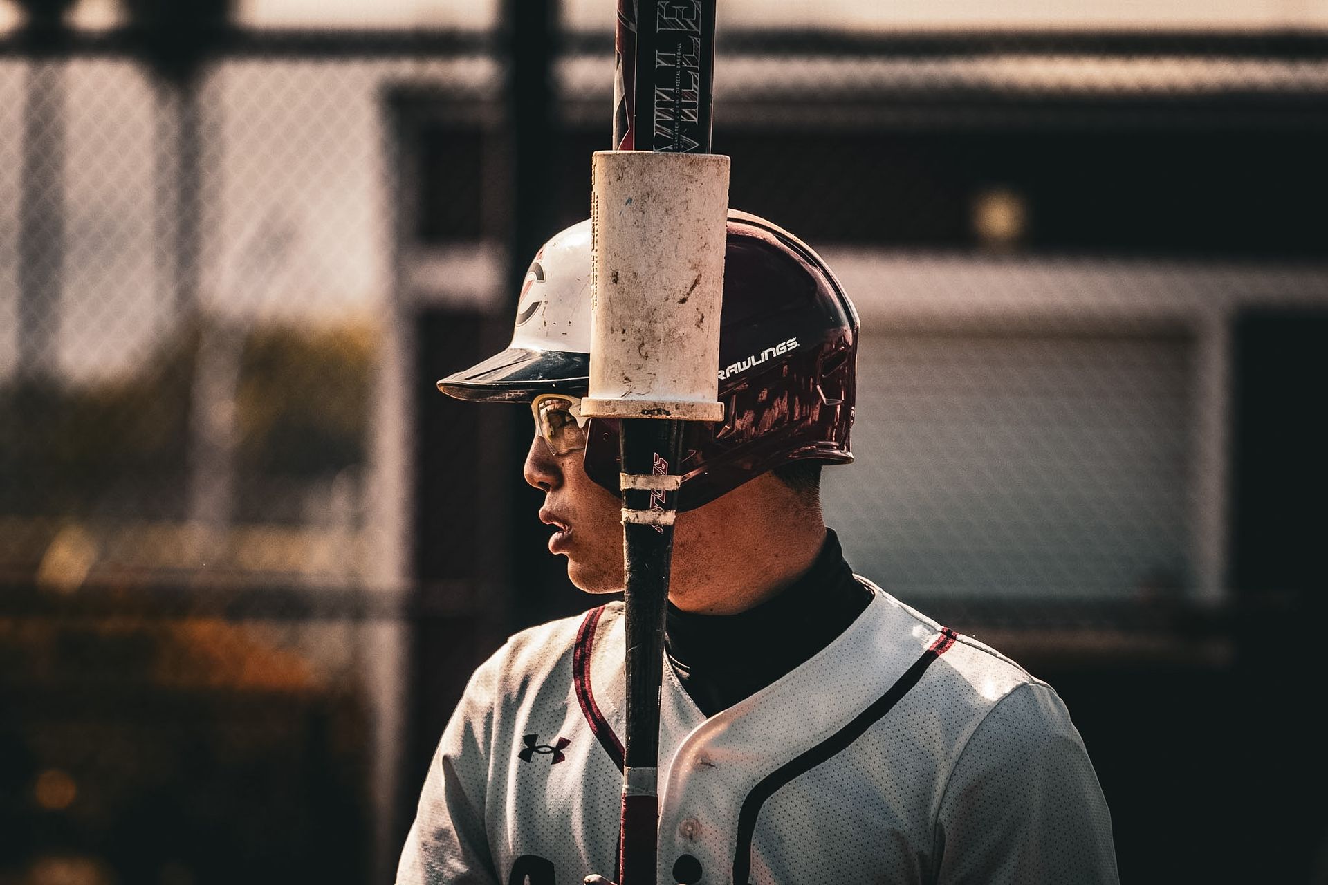 Baseball player in gray uniform and helmet standing at the plate, seen in profile behind a bat.