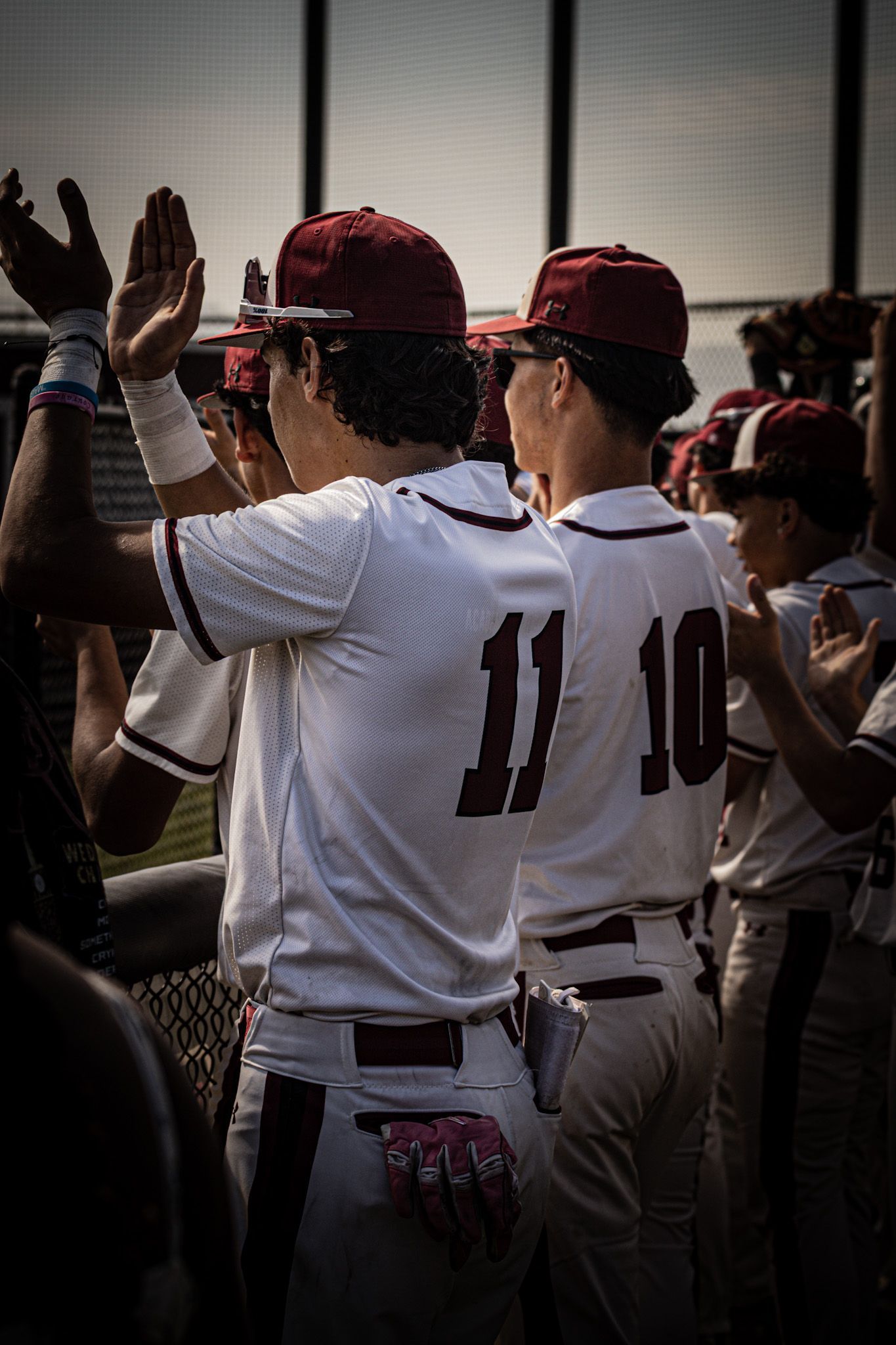 Baseball players in maroon caps and white jerseys cheering by a fence, hands raised in celebration
