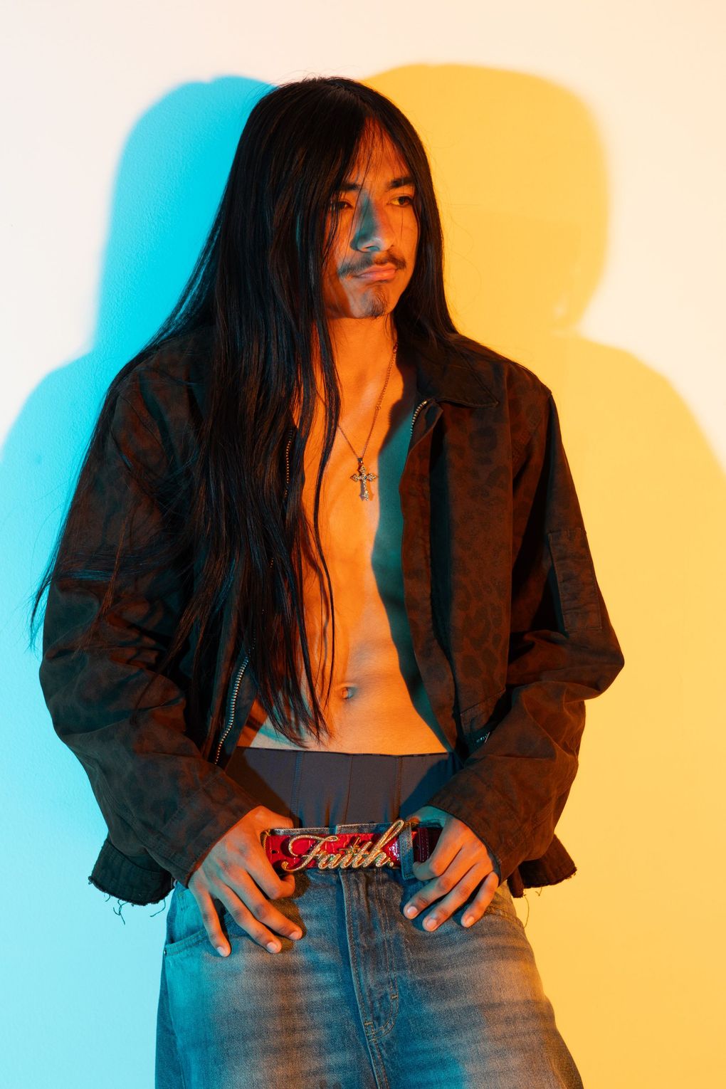 Fashion studio portrait of a man in an open jacket against a striking yellow and blue split-color background.