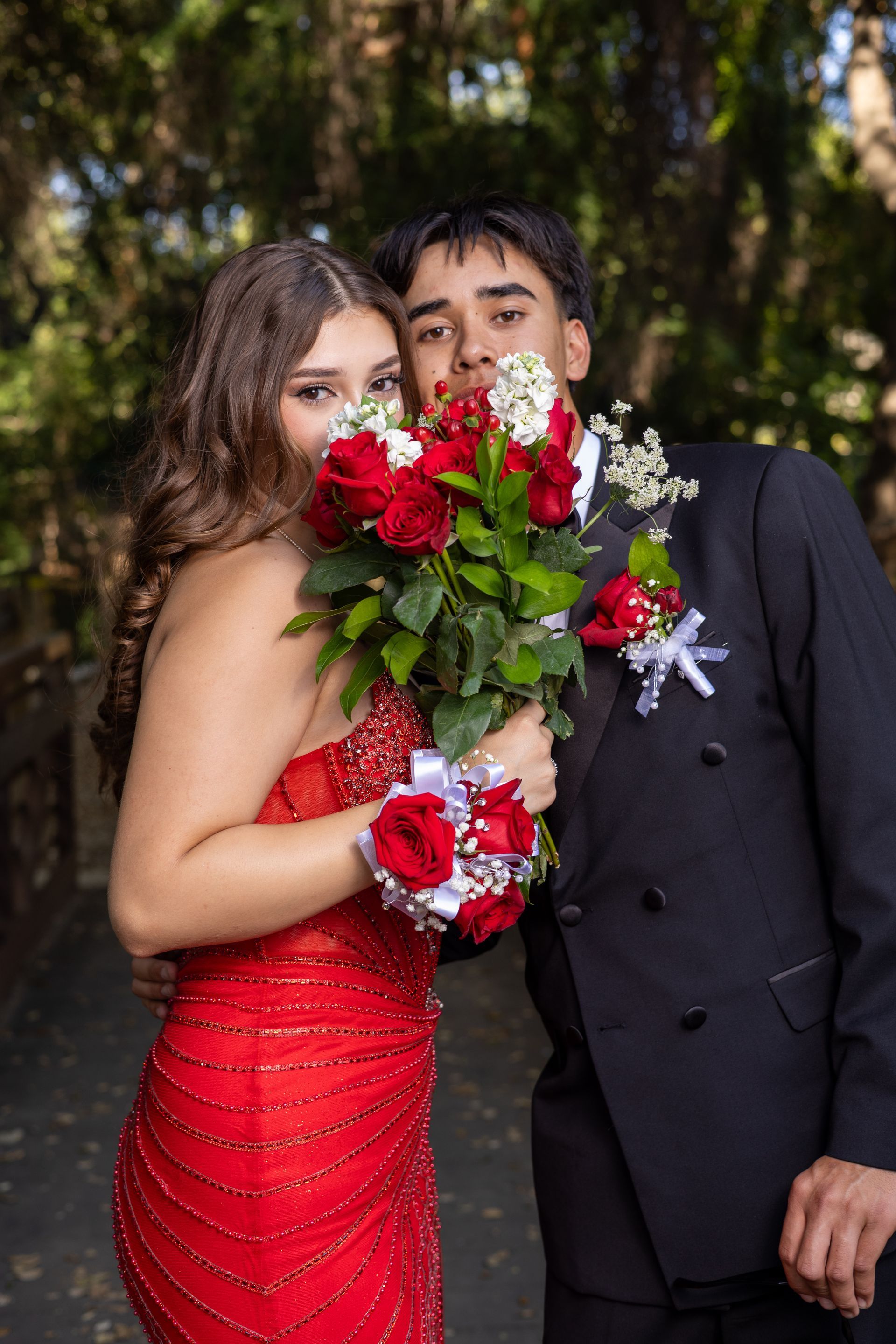 Couple in formal wear holding a bouquet of red roses outdoors