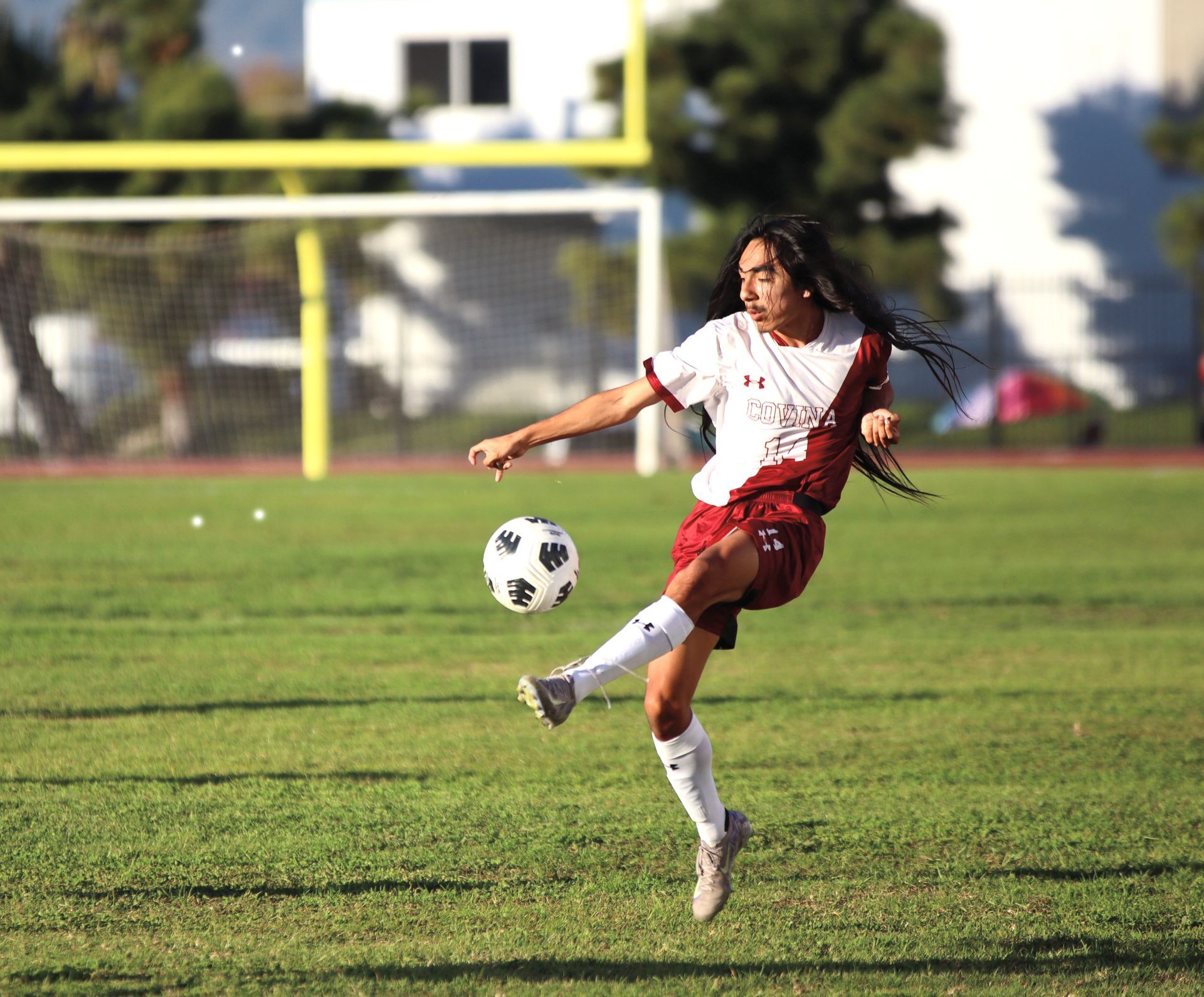 Soccer player in white and red kicks a ball on a grassy field near the goal area