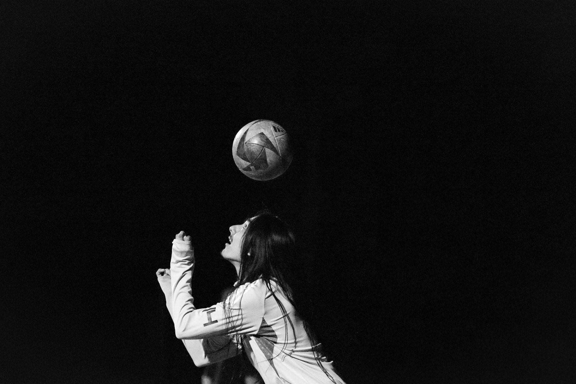Woman in a striped shirt balancing a soccer ball on her head against a dark background