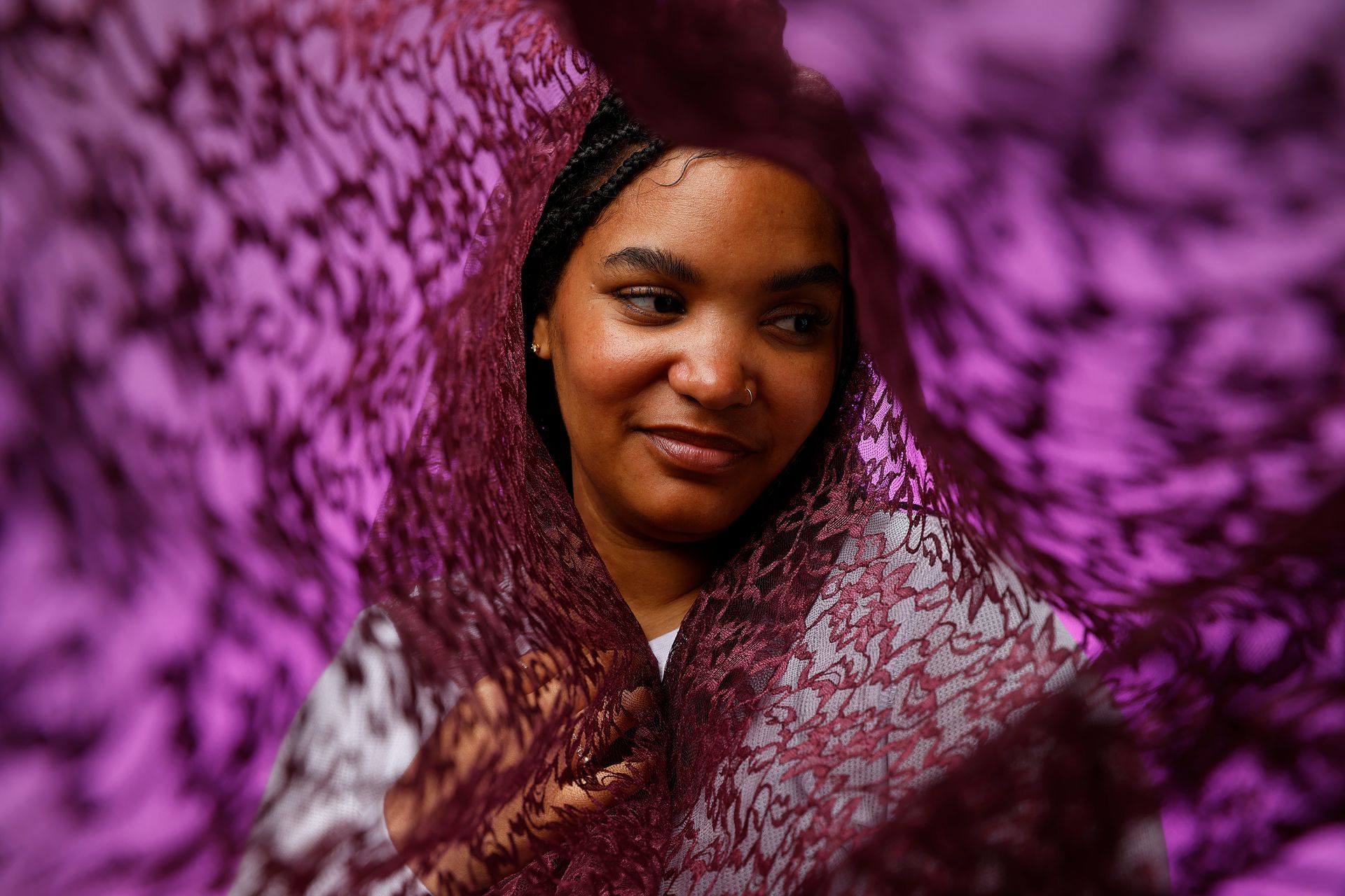 Person looking through purple lace fabric, with a soft smile.