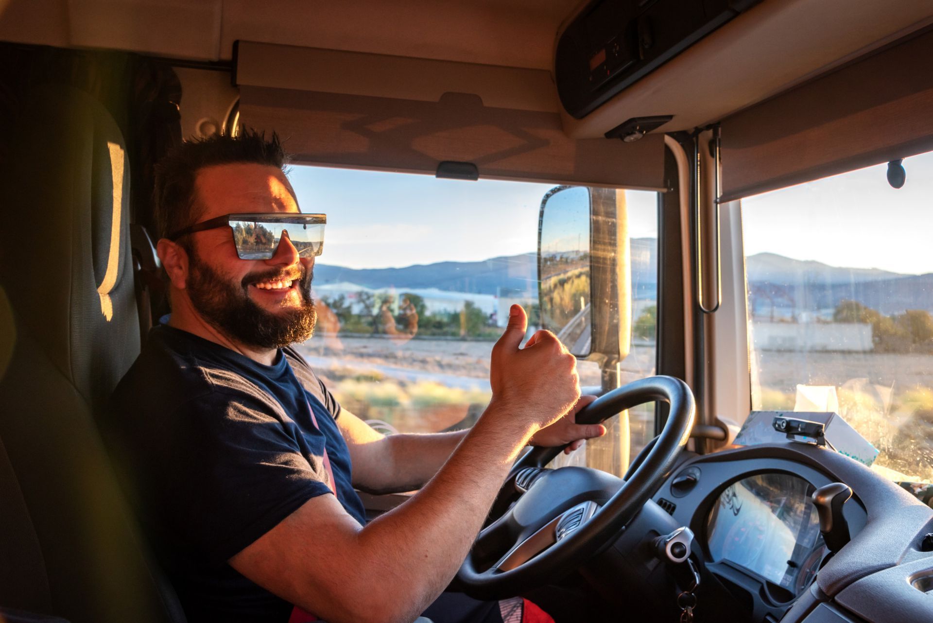 A man is sitting in the driver 's seat of a truck giving a thumbs up.