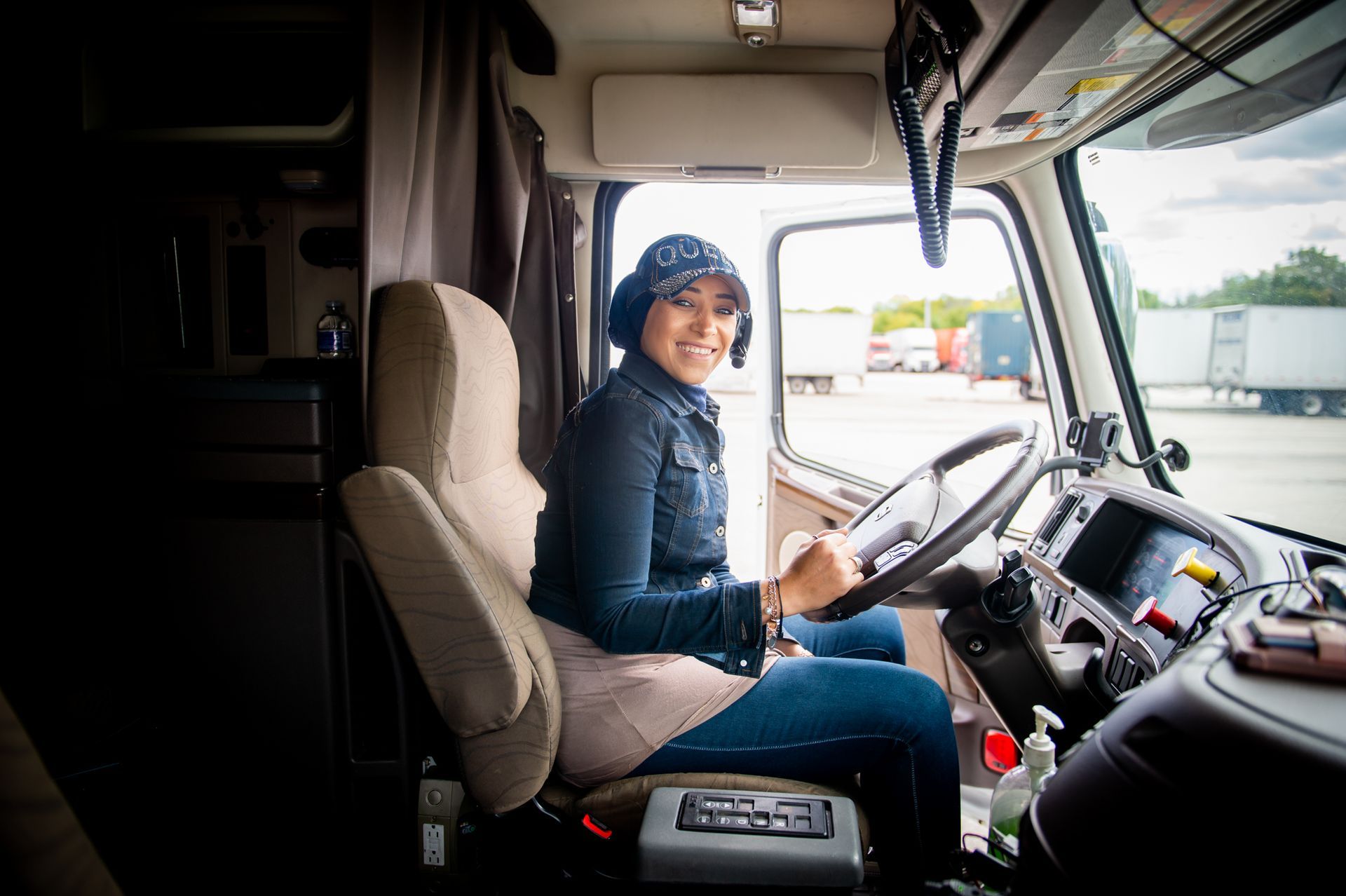A person smiling while sitting in the driver's seat of a truck, gripping the steering wheel in a parking lot.