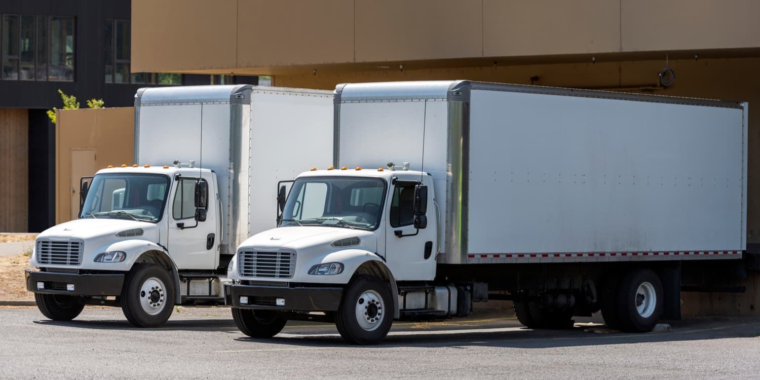 Two white trucks are parked next to each other in a parking lot.