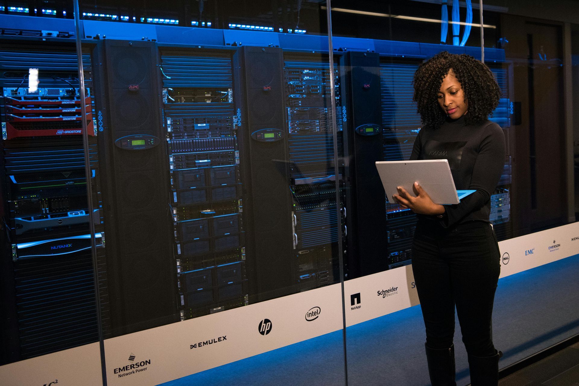 A professional works on a laptop in front of a row of illuminated server racks in a data center.