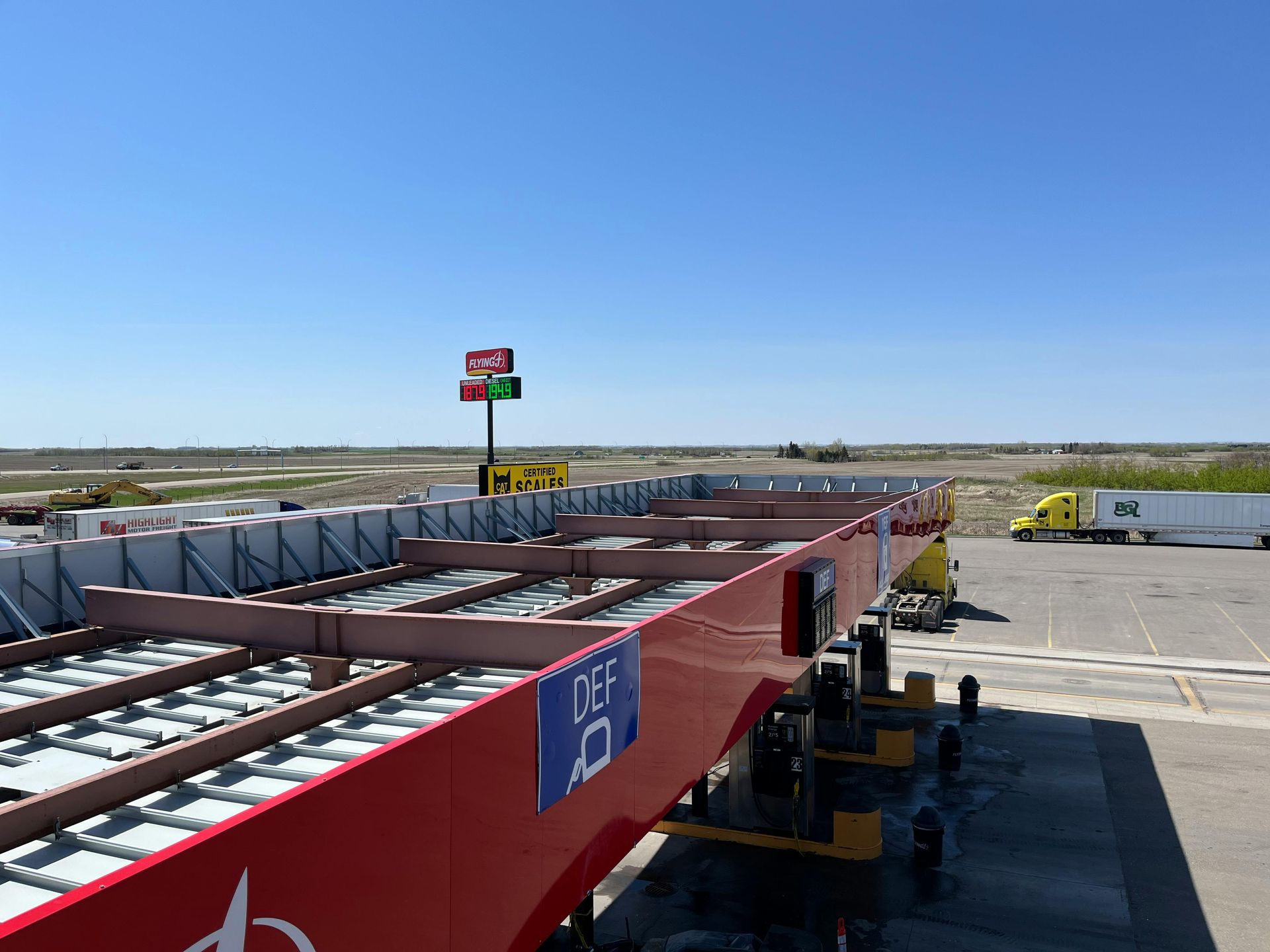 Red truck trailer parked, sign with numbers, blue sky, concrete ground, and distant landscape.