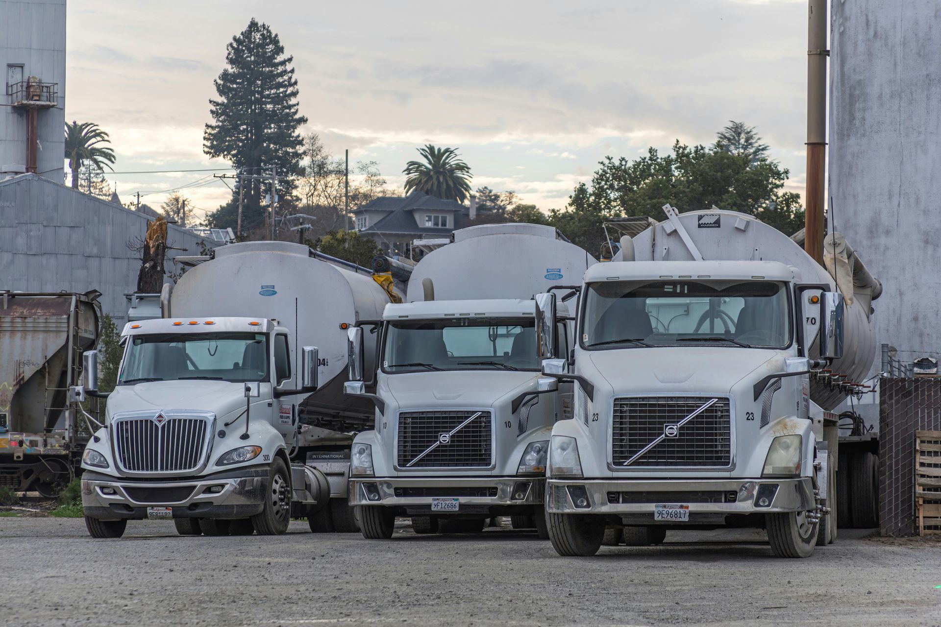 Three tanker trucks parked outdoors near industrial buildings.