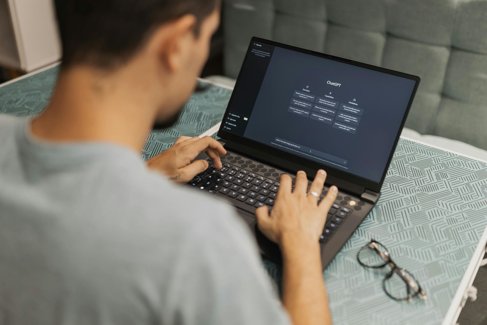 Person typing on a laptop displaying a hierarchical diagram, with glasses resting on a patterned table nearby.