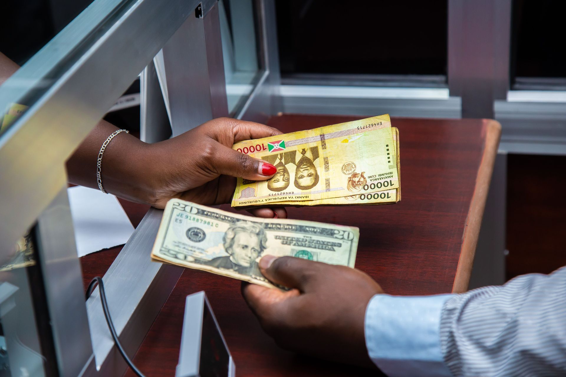 Two hands exchanging U.S. and Zimbabwe banknotes across a glass counter